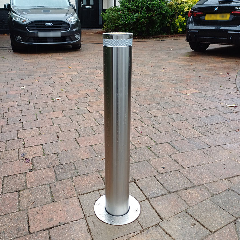 Stainless steel automatic bollard installed on a block paved driveway.