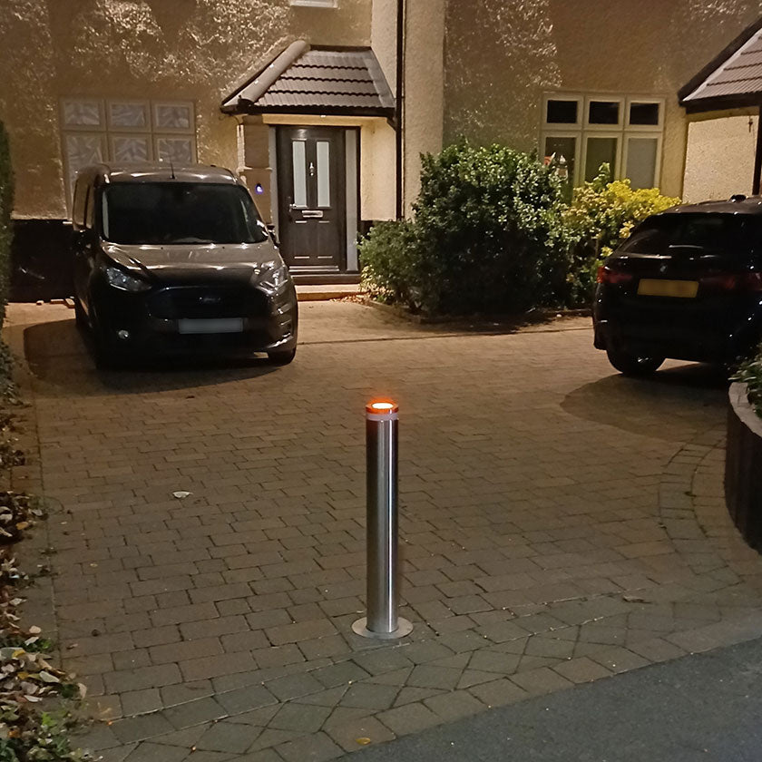 Bollard light on a driveway with cars and a house in the background