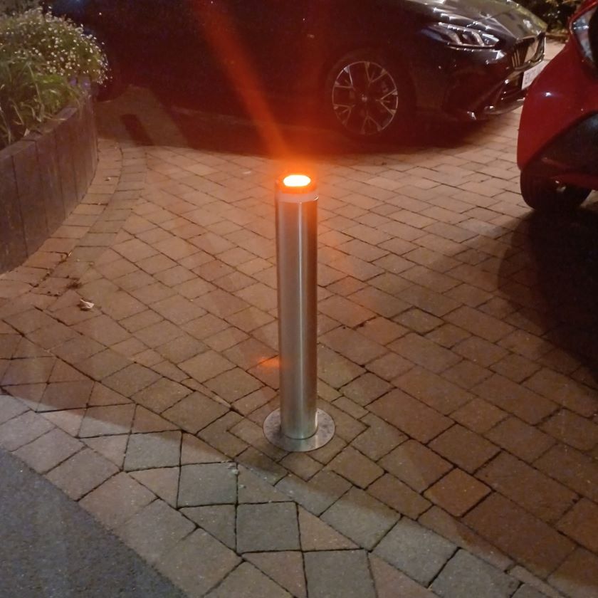 Bollard lighting on a paved driveway with cars in the background