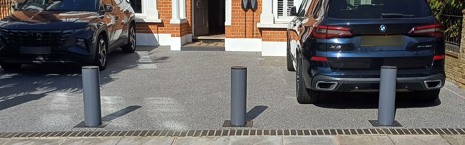 Two cars parked on a driveway with BFT automatic rising bollards across the entrance.