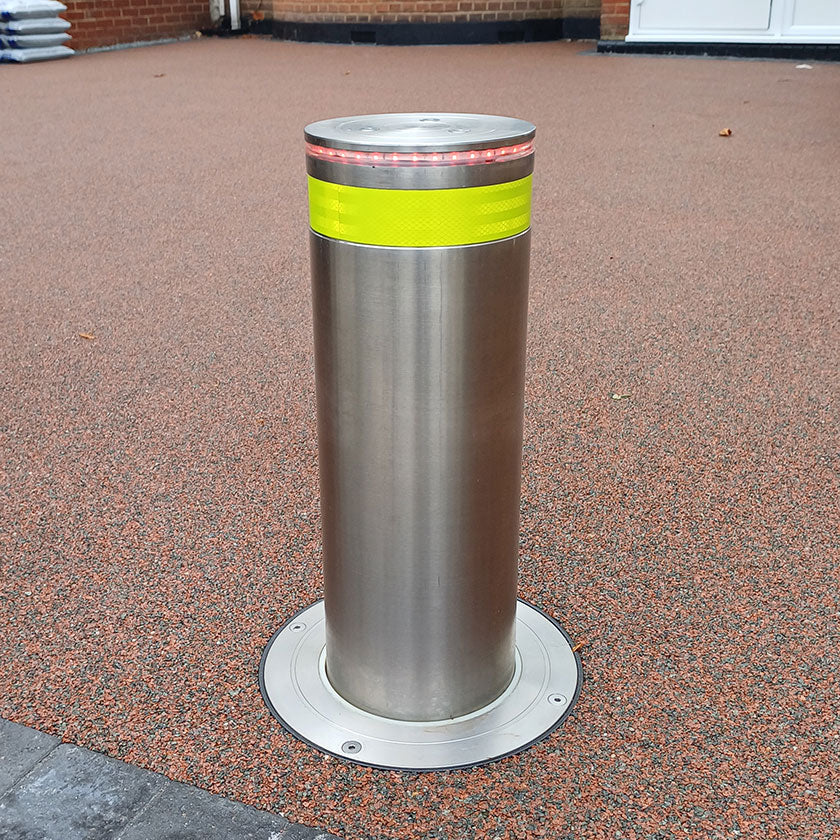 Stainless steel automatic rising bollard  with a Yellow reflective band on a resin bound driveway.
