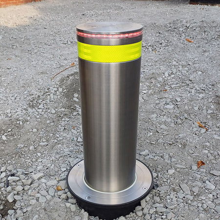 Stainless steel automatic rising bollard  with a Yellow reflective band on a driveway with a type 1 sub-base