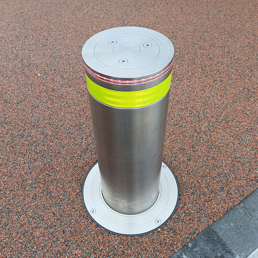 Stainless steel automatic rising bollard  with a Yellow reflective band on a resin bound driveway.