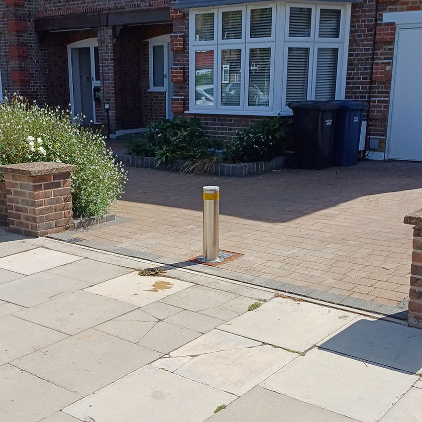 Paved driveway with a stainless steel automatic bollard and brick building in the background