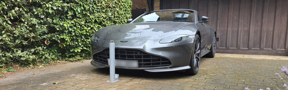 High security telescopic bollard installed in front of a Grey sports car parked on a driveway next to a wooden fence and greenery.